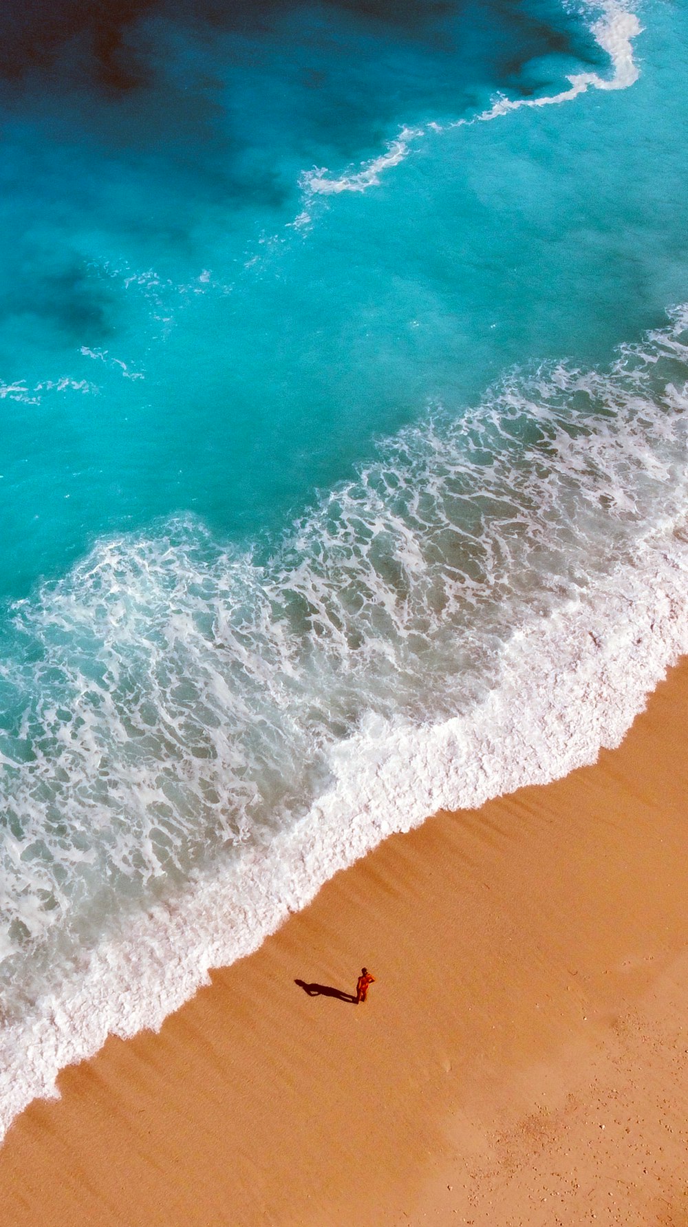 an aerial view of a beach with a person walking on the sand