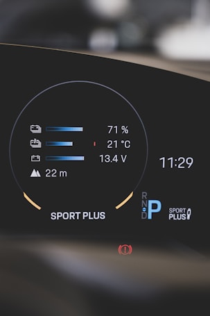 A modern car dashboard displaying various metrics such as battery level at 71%, temperature at 21°C, and voltage at 13.4V. The dashboard also shows a gear indicator with 'P' for park, the mode 'Sport Plus', a warning icon, and the time 11:29.