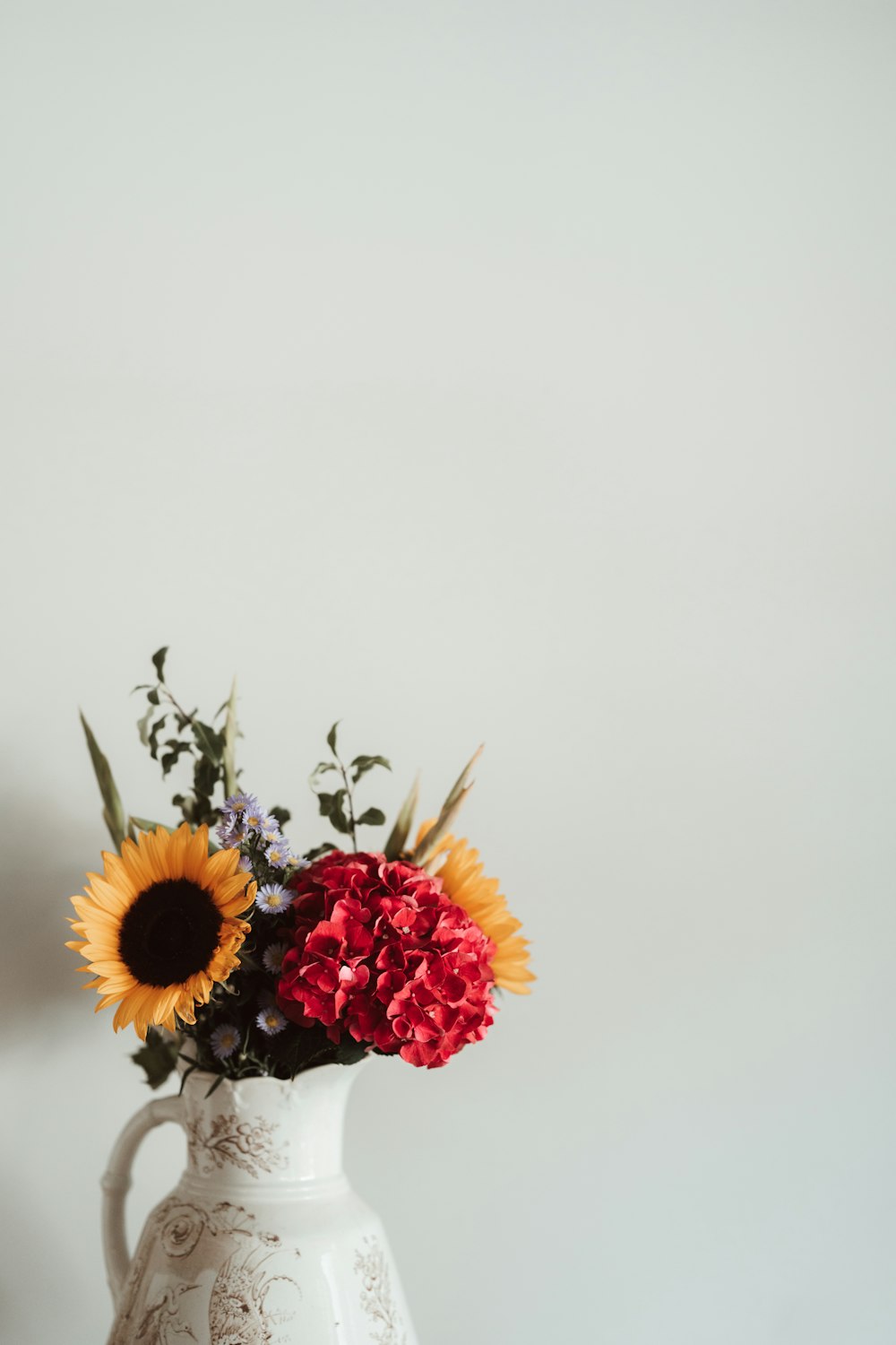 a white vase filled with red and yellow flowers