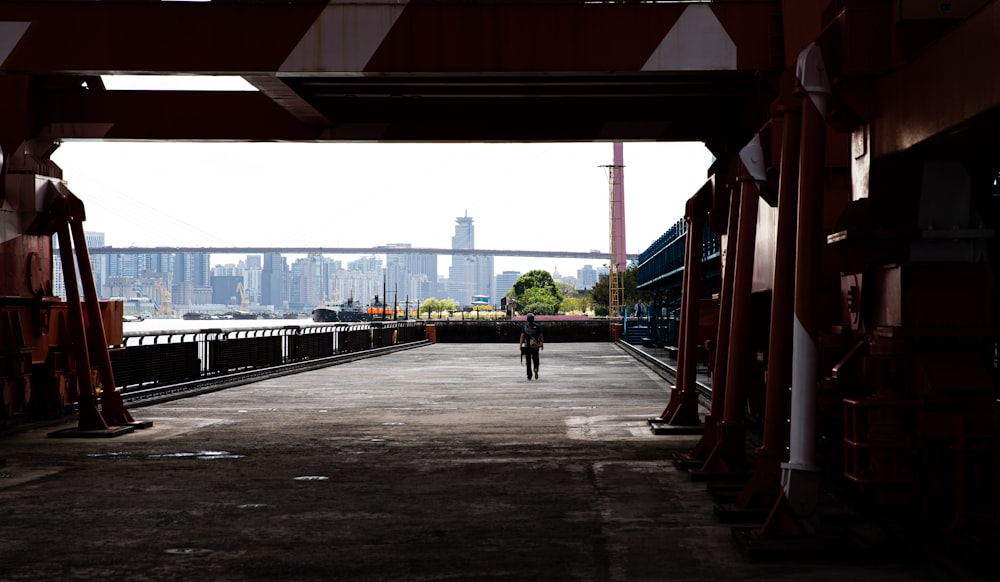 a person walking down a walkway in front of a bridge