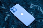 A smartphone with a prominent logo is lying on a dark patterned surface. The phone has a smooth, sleek design with dual rear cameras.