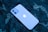 A smartphone with a prominent logo is lying on a dark patterned surface. The phone has a smooth, sleek design with dual rear cameras.