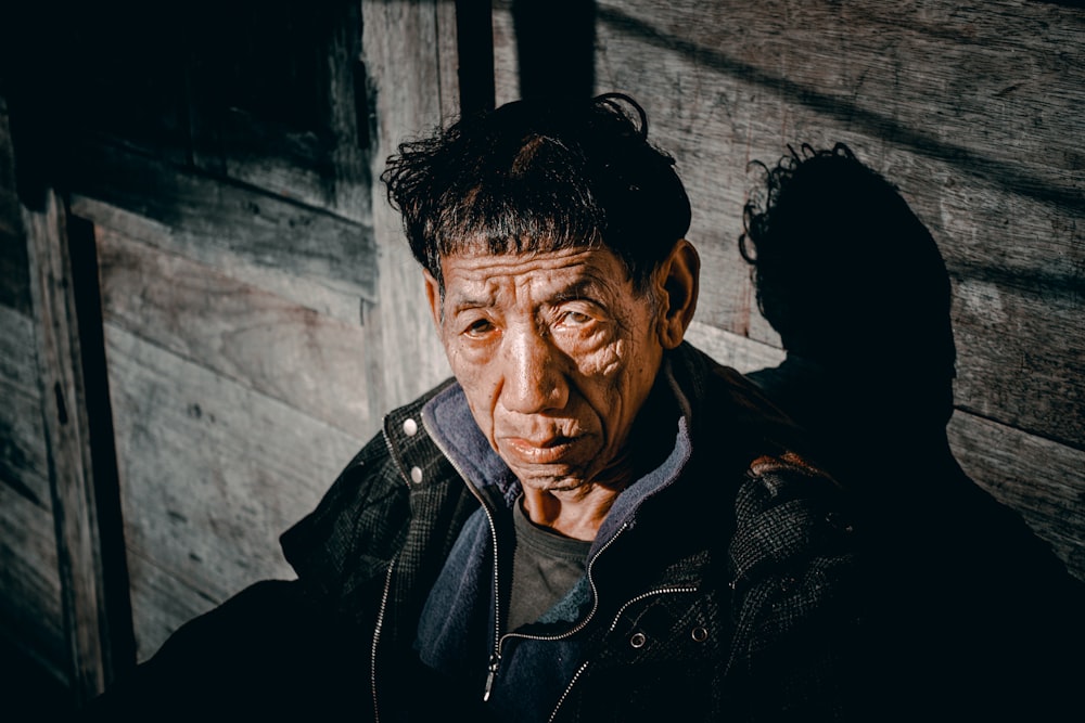 an old man is standing in front of a wooden wall