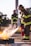 Firefighters in gear actively participate in a training exercise, using fire extinguishers to control and suppress a controlled fire. Protective helmets and reflective stripes on uniforms are visible, emphasizing safety protocols.