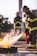Firefighters in gear actively participate in a training exercise, using fire extinguishers to control and suppress a controlled fire. Protective helmets and reflective stripes on uniforms are visible, emphasizing safety protocols.
