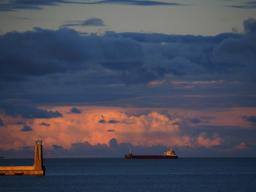 a large cargo ship in the distance with a lighthouse in the foreground