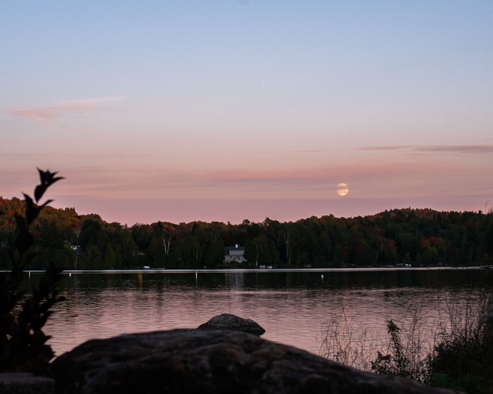 the moon is setting over a lake with trees in the background