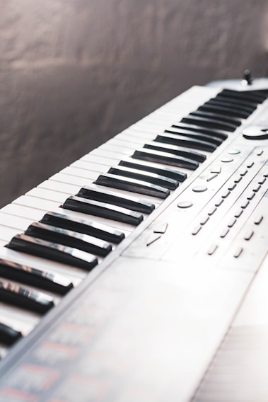 A close-up of a musical keyboard, showing an array of black and white keys with buttons and control knobs on the side. The keyboard is positioned diagonally in the frame, creating a dynamic perspective.