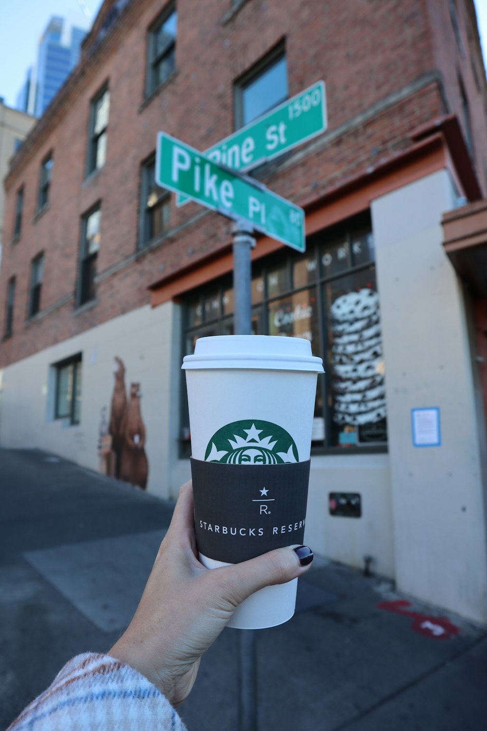 a person holding a cup of coffee in front of a street sign