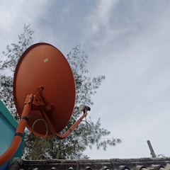 A large orange satellite dish mounted on a roof with trees in the background under a partly cloudy sky.