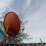 A large orange satellite dish mounted on a roof with trees in the background under a partly cloudy sky.