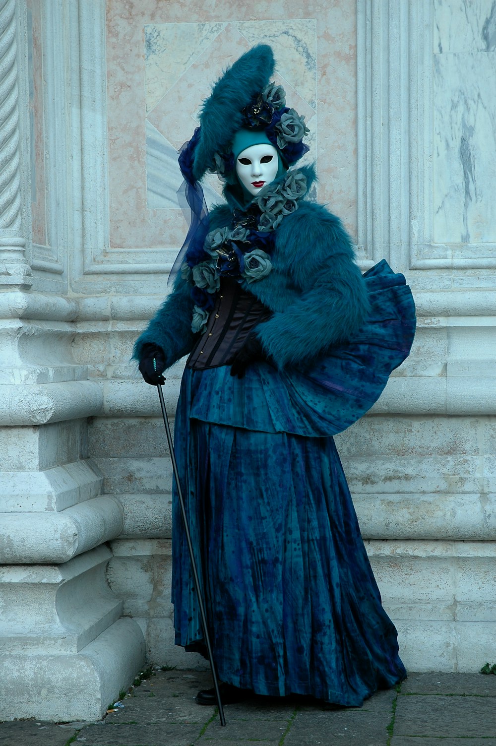 a woman in a blue dress with a mask and a cane