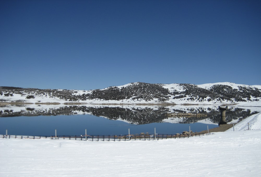 a lake surrounded by snow covered mountains and a fence
