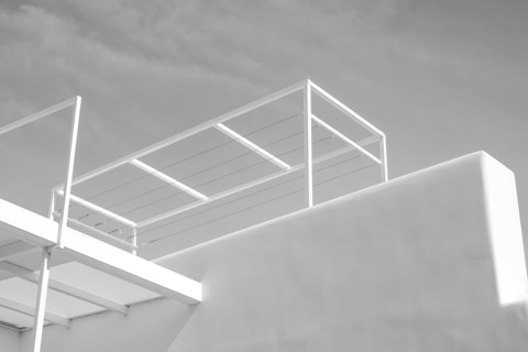 An architectural structure with clean, minimalist lines featuring white panels and railings set against a grey sky. The design emphasizes simplicity and modernity.