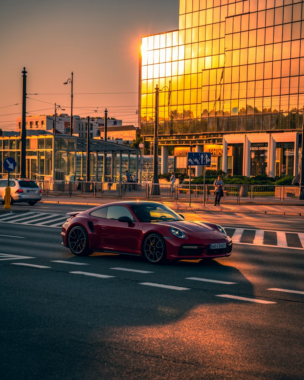 a red sports car driving down a street next to a tall building