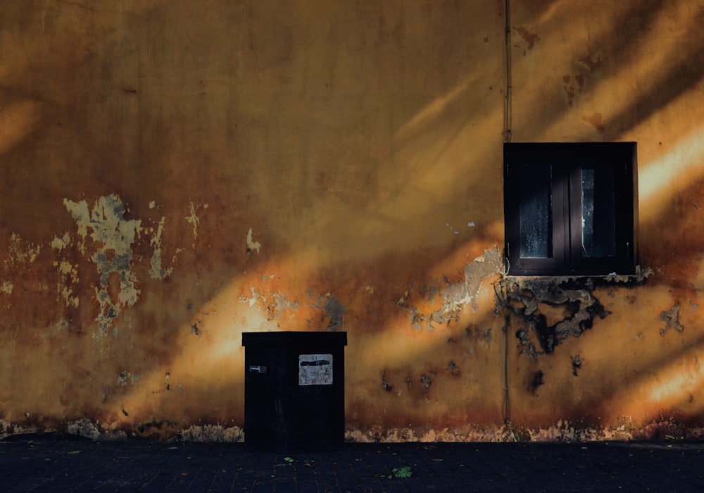 a yellow wall with two windows and a trash can