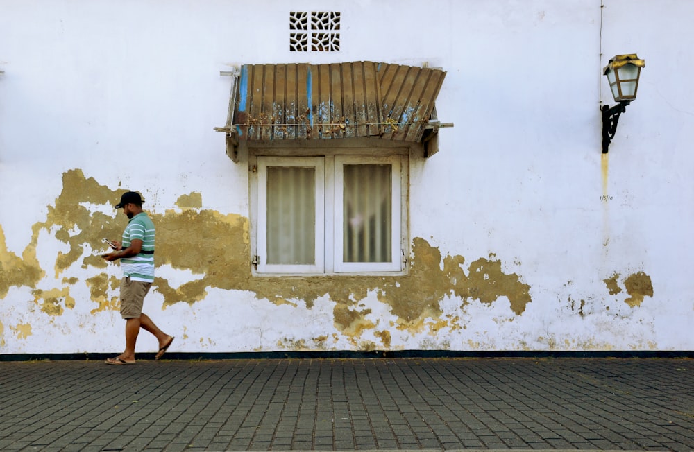 a man walking down a street past a white building