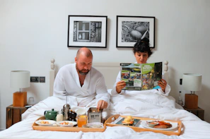 a man and woman sitting on a bed reading a magazine