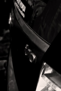 A close-up shot of the rear section of a car with an Audi logo visible, along with part of a dealership sticker on the window. The tail light is partially visible and the car appears to be black, with reflections suggesting a glossy finish.