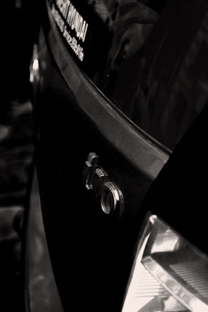 A close-up shot of the rear section of a car with an Audi logo visible, along with part of a dealership sticker on the window. The tail light is partially visible and the car appears to be black, with reflections suggesting a glossy finish.