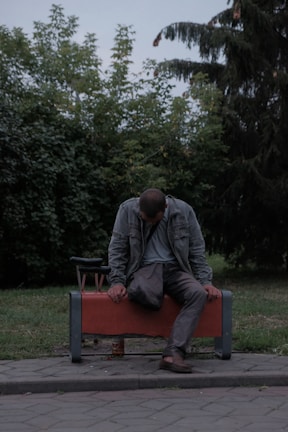A tired man sitting alone at dawn in an urban setting, looking lost and drained