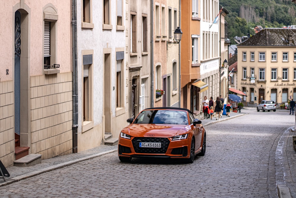 an orange car is parked on a cobblestone street