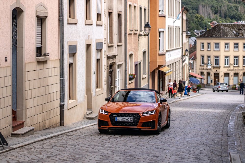 Une voiture orange est garée dans une rue pavée
