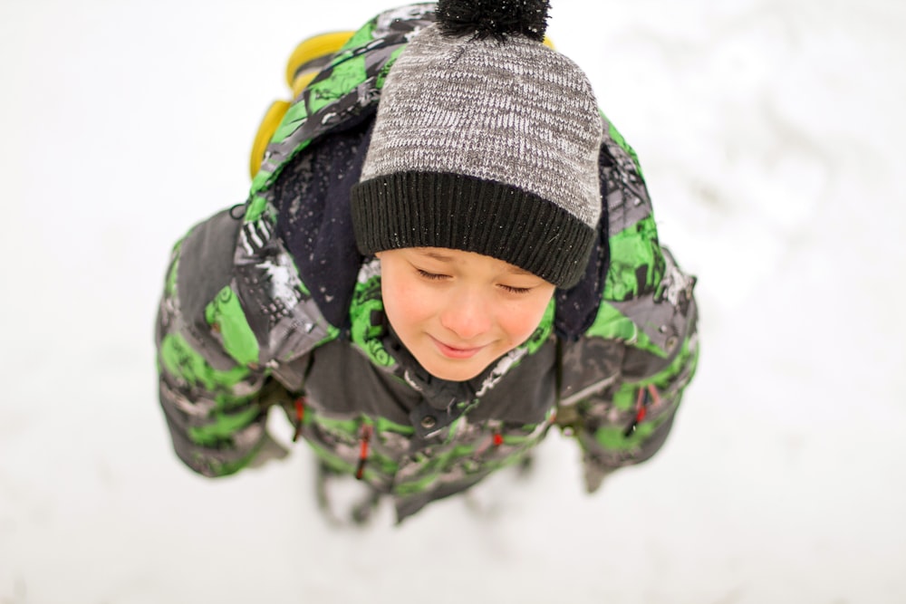 Un niño con una chaqueta verde y negra y un sombrero gris y negro