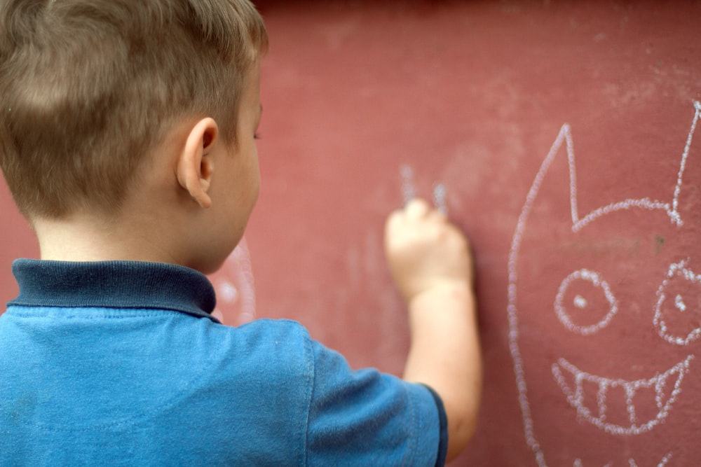 Ein kleiner Junge schreibt mit einem Filzstift an eine Wand