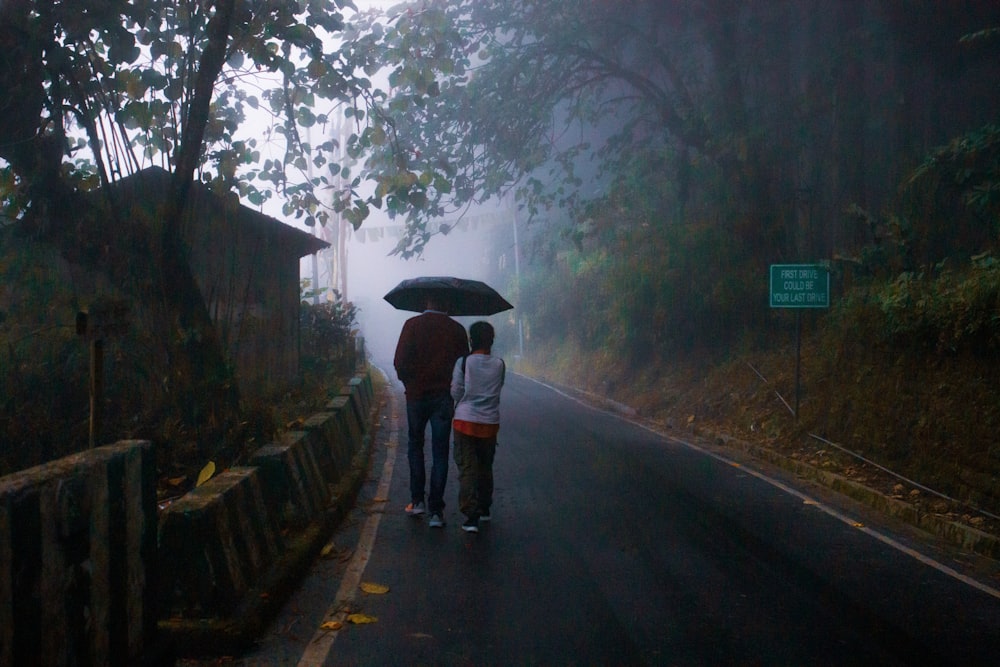 two people walking down a road with an umbrella