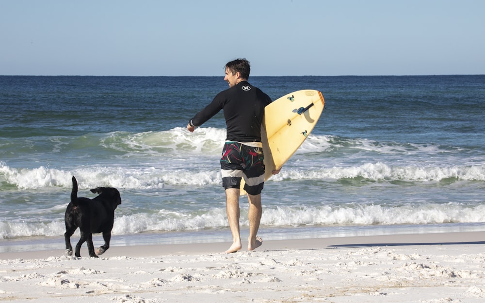 um homem com uma prancha de surf e um cão na praia