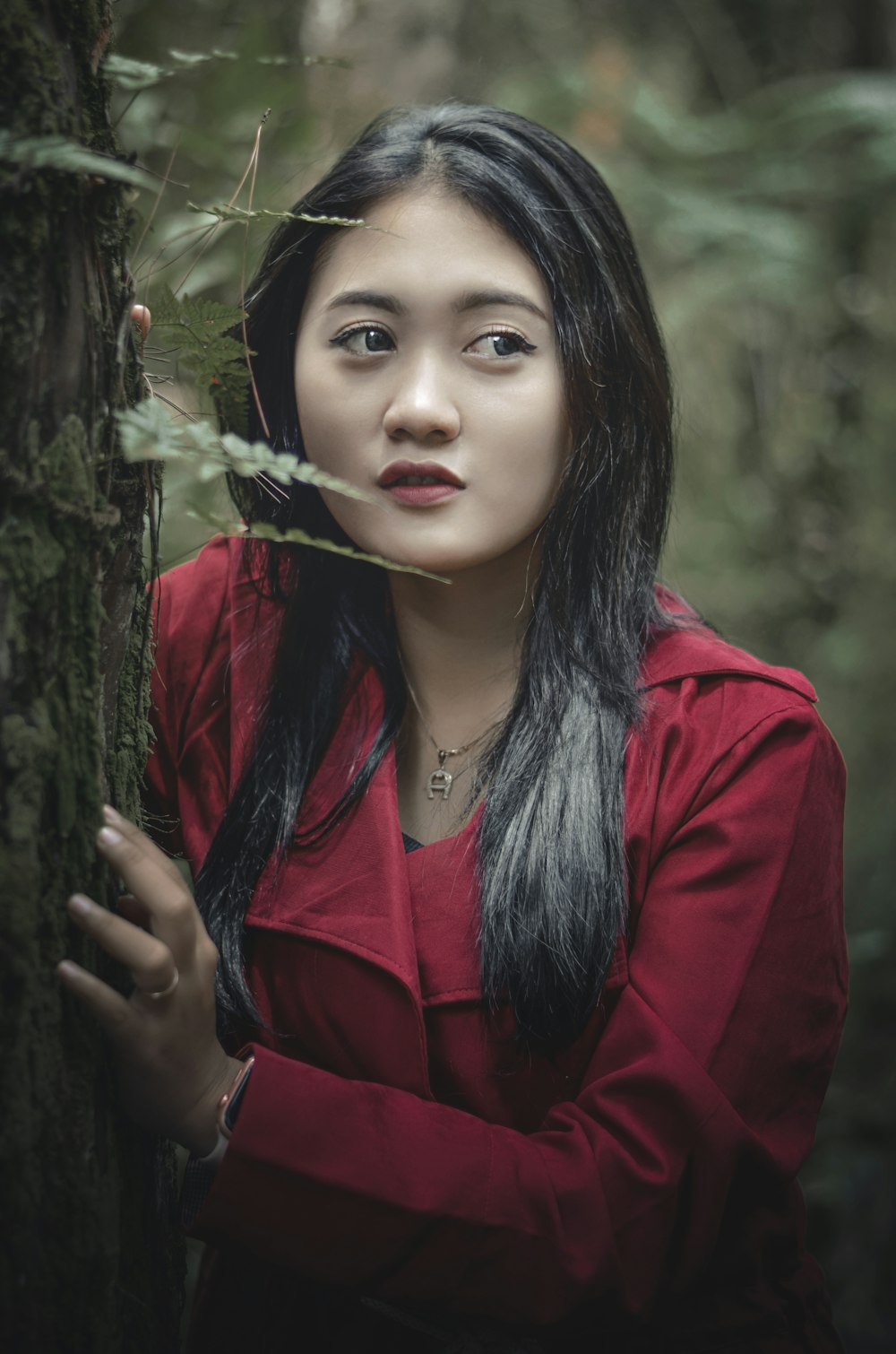 a woman in a red shirt leaning against a tree