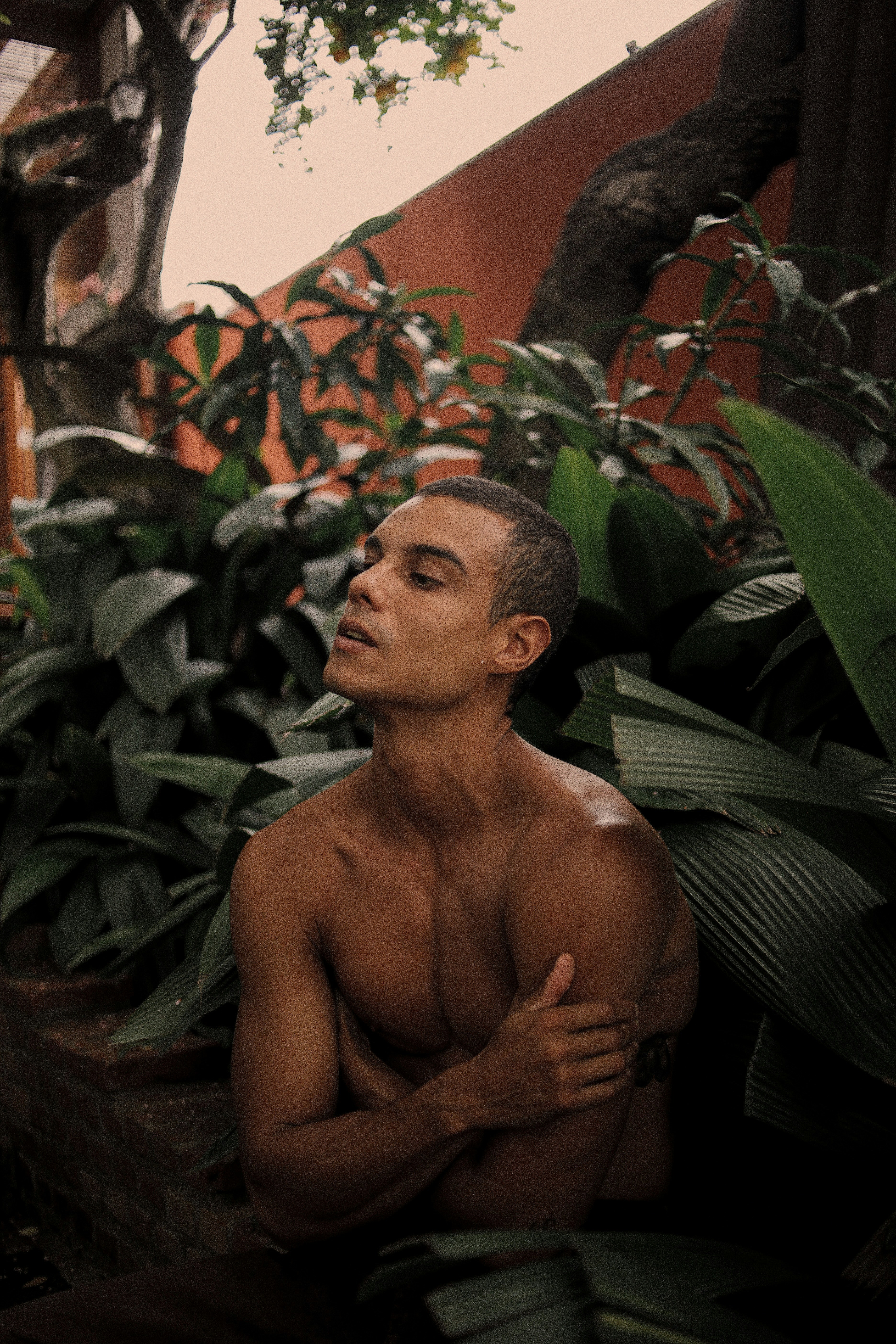 a shirtless man sitting in front of some plants