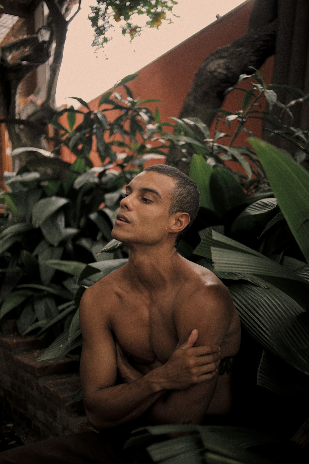 a shirtless man sitting in front of some plants