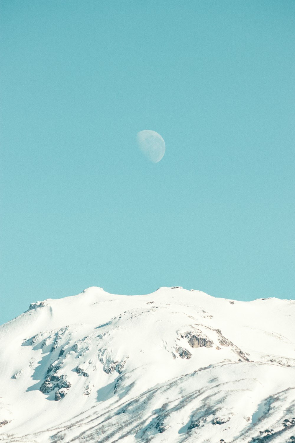 a snow covered mountain with a half moon in the sky