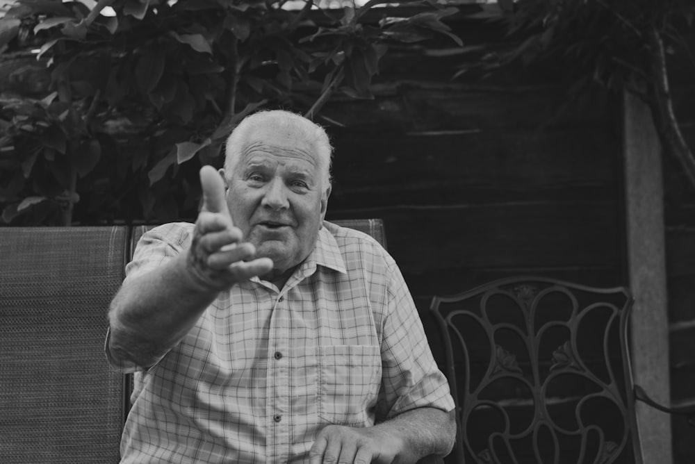 an older man sitting in a chair making a peace sign