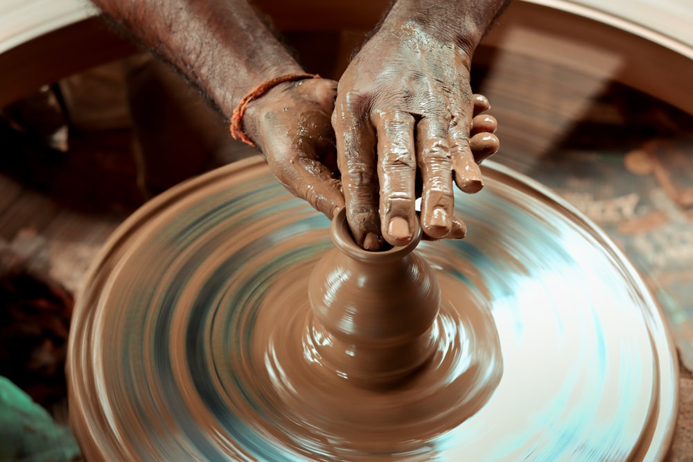 uma pessoa fazendo um vaso na roda de um oleiro