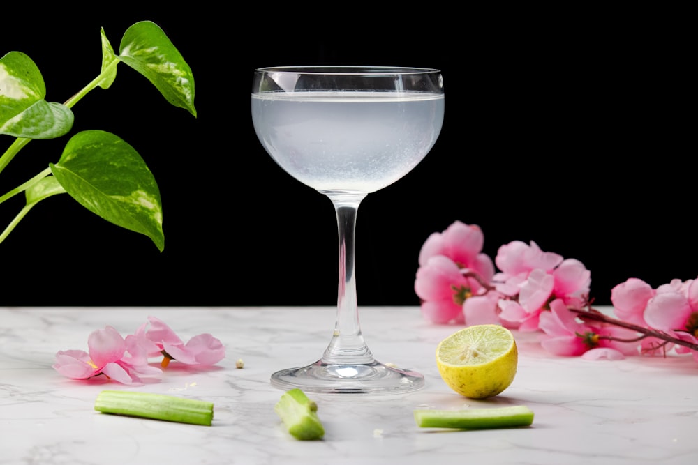 a glass of water next to a lemon slice and flowers