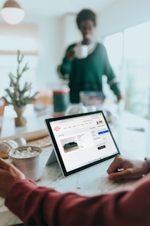Person on their Surfacelaptop online shopping drinking hot chocolate with person in background out of focus