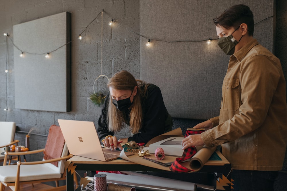 Two coworkers wearing masks wrapping presents and looking at a Surface laptop 