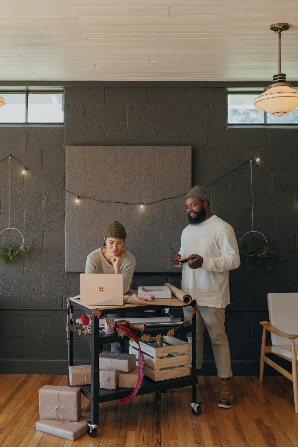 Two coworkers on a Surface laptop with Christmas presents on a cart 