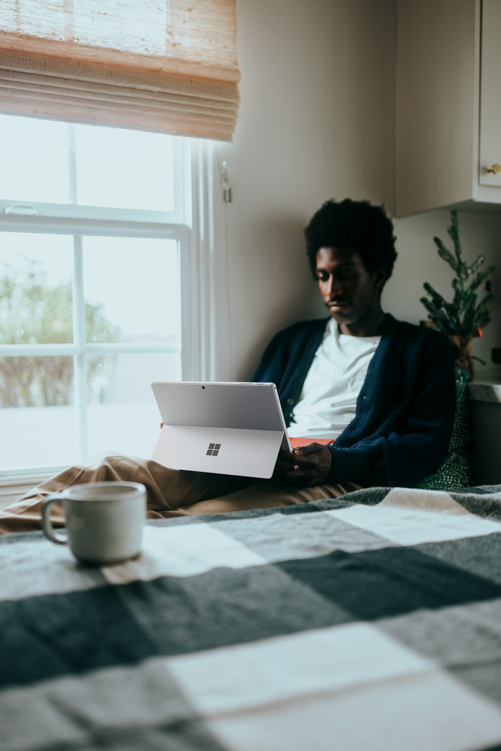 Man sitting by a window on his Surface laptop, Christmas tree in the background