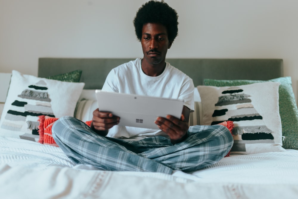 Homme sur son lit sur son ordinateur portable Surface avec des oreillers de vacances derrière 