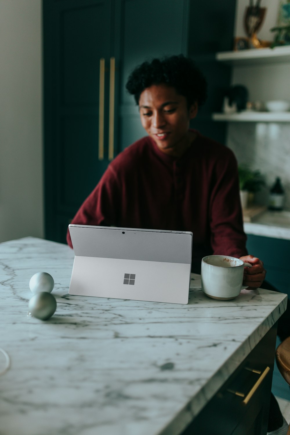 キッチンのテーブルに座って、Surface ノート PC でコーヒーを飲んで何かを見ている男性