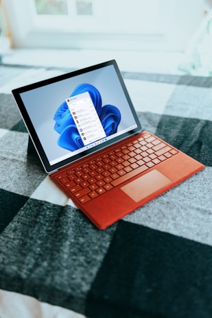 Red Surface laptop on a checkered bed by a window 