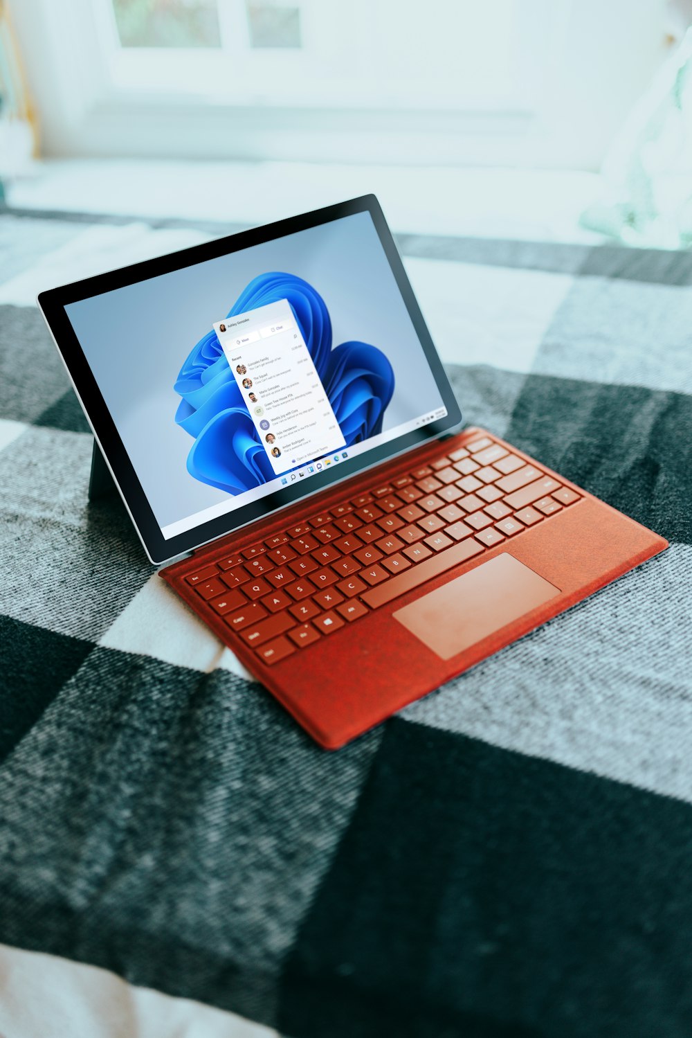 Red Surface laptop on a checkered bed by a window 