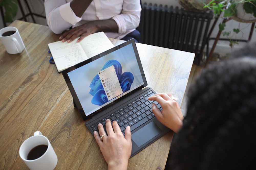 Ansicht von oben von zwei Personen an einem Tisch, die mit einem Microsoft-Laptop und -Notebook arbeiten