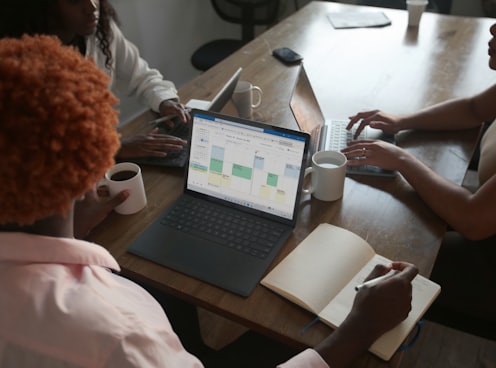 Three people in a meeting at a table discussing schedule on their Microsoft laptop