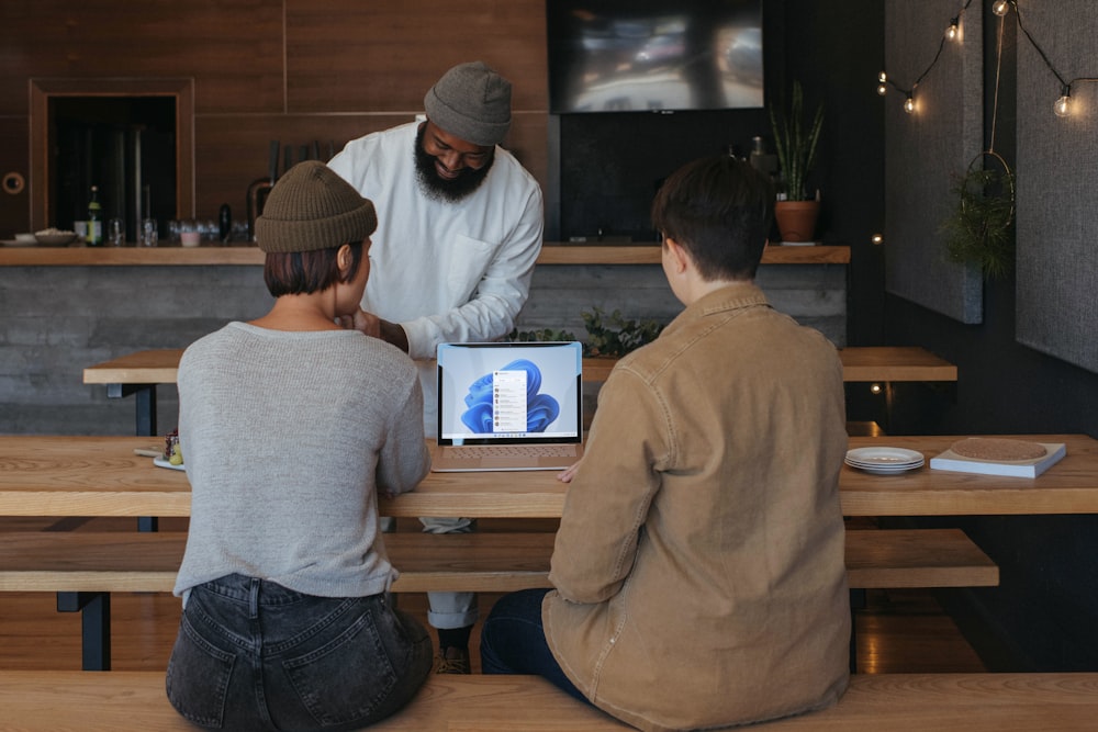 Tres personas sentadas en bancos trabajando alrededor de una computadora portátil de Microsoft 