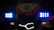 The image displays the front of a vehicle or bike adorned with bright LED lights. Blue and orange lights are prominent next to a central logo or emblem which features a red star and text. The lighting creates a high-contrast effect against the dark background.